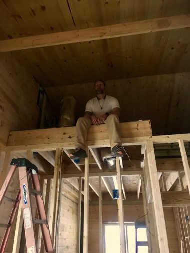 man sitting in loft being framed in with tongue and groove ceiling