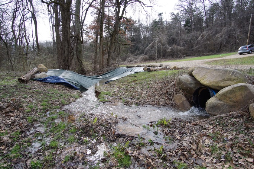 creek running from conduit into sinkhole under tarp