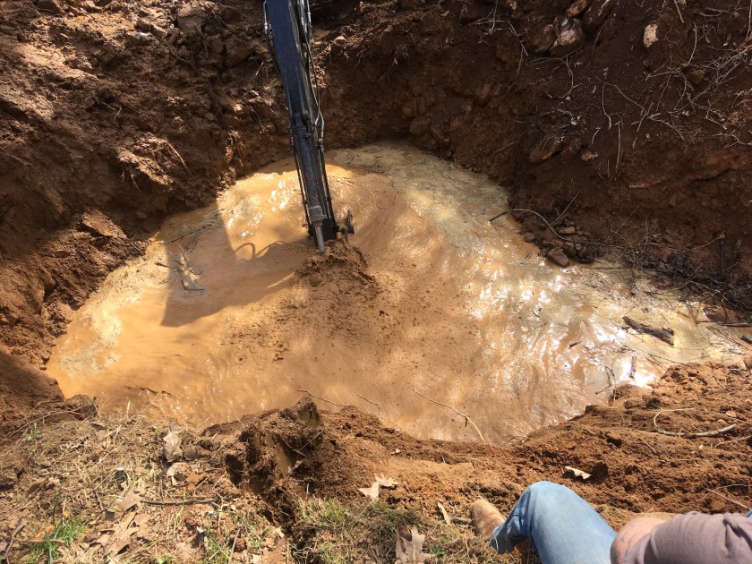excavator digging in muddy water by man's knee and shoulder