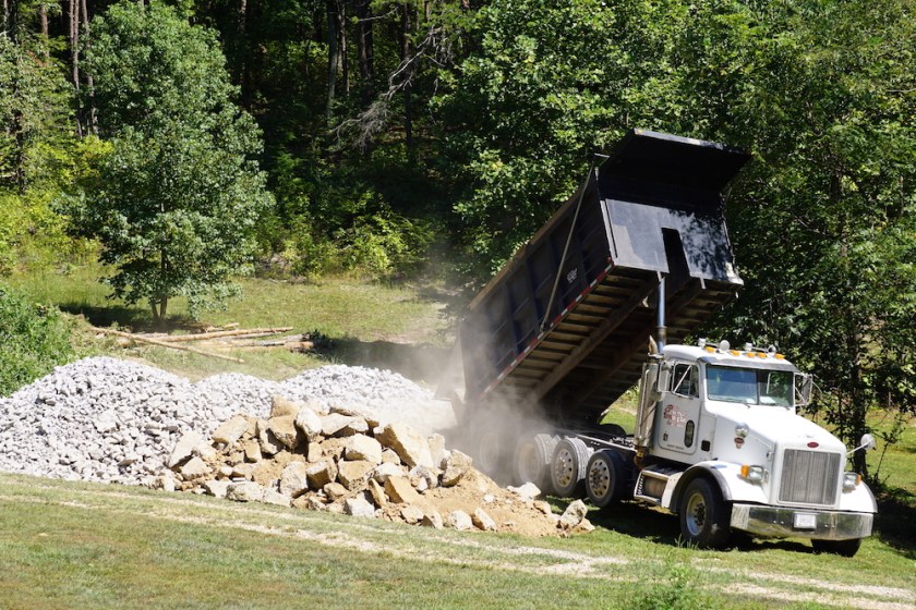 dumptruck delivering dusty rocks on green grass